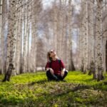 woman sitting in the grass in front of threes